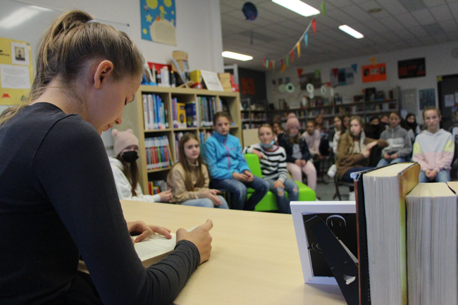 Schülerin liest im Vordergrund, Klasse hört zu
