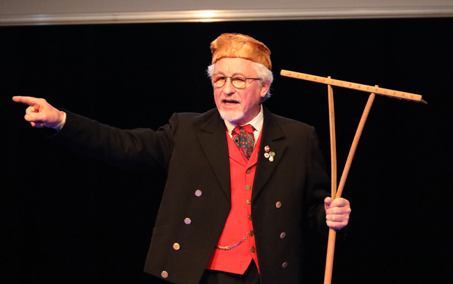 Mann in Tracht mit Rechen in der Hand gestikulierend
