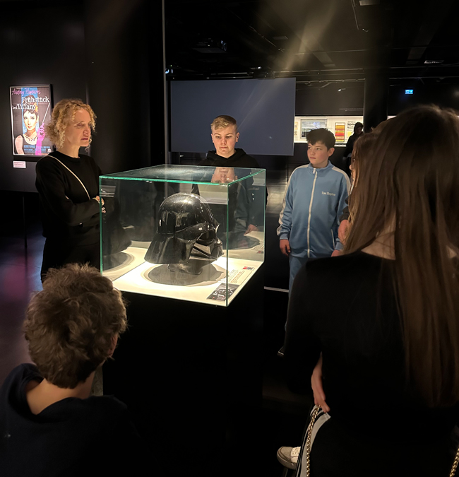 Schüler stehen um Glasvitrine mit Helm von Darth Vader