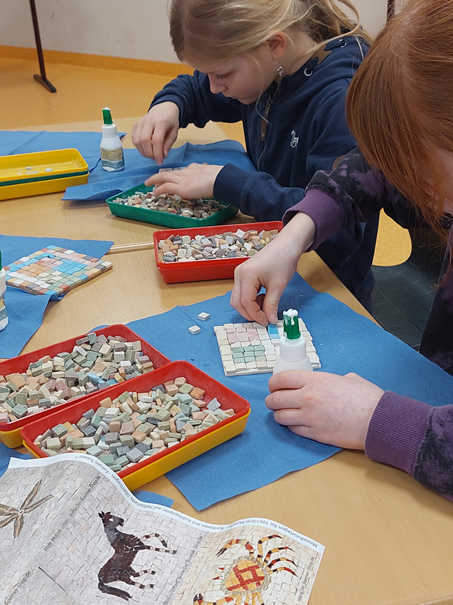 Schüler kleben Mosaiksteinchen auf Platten