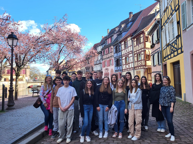 Gruppenbild vor bunten Häusern und blühenden Bäumen vor blauem Himmel