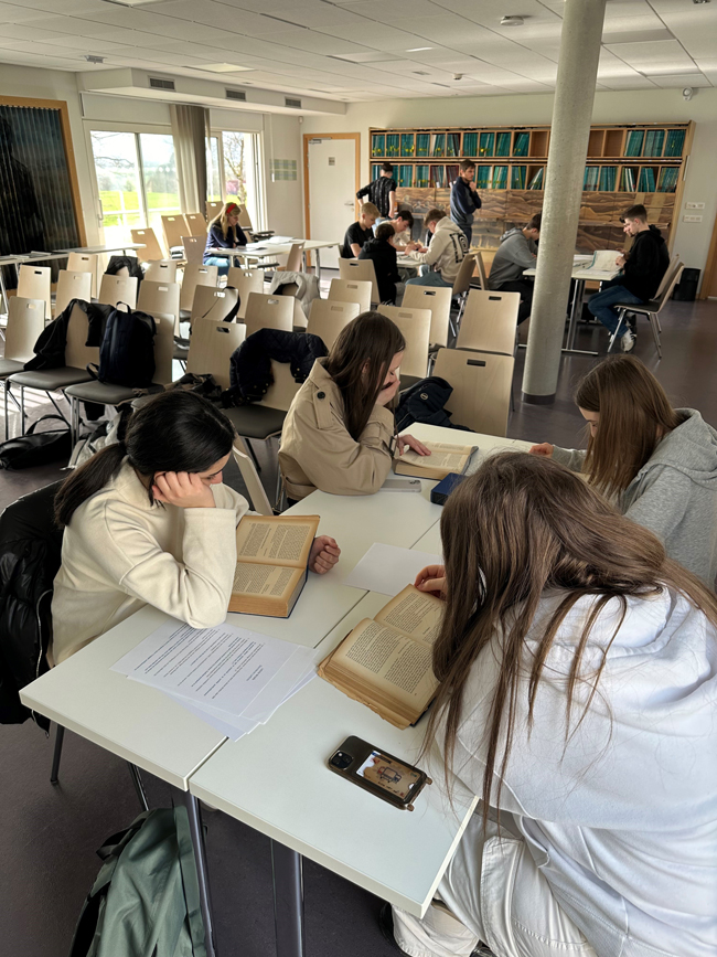 Schüler, die in einem Raum in Bücher vertieft an Tischen sitzen