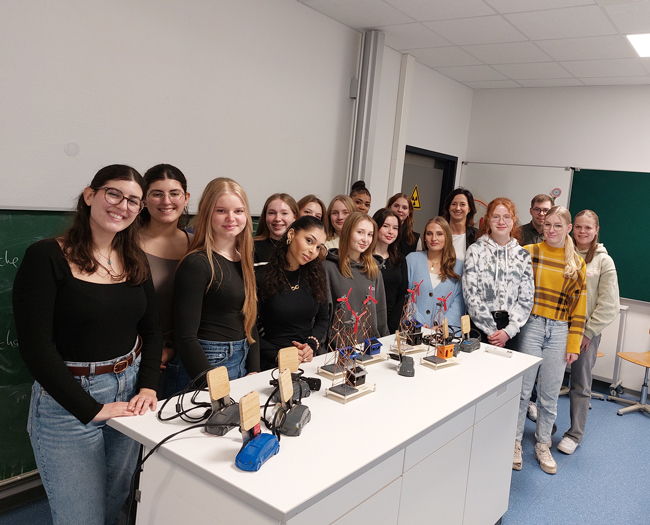 Gruppenbild der Teilnehmerinnen des Projektes am Lehrertisch, der mit den selbstgebauten Autos und Windrädern der Praxistage voll steht