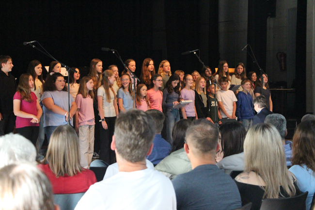Schülerchor mit circa 30 Jungen und Mädchen singend auf der Bühne