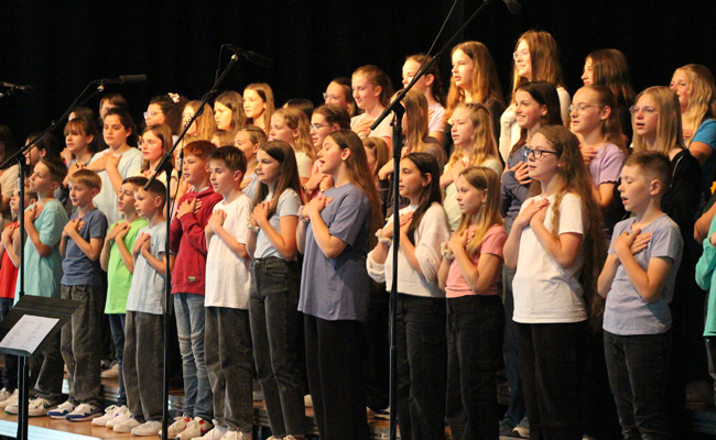 großer Chor singend, Schüler halten beide Hände auf ihr Herz