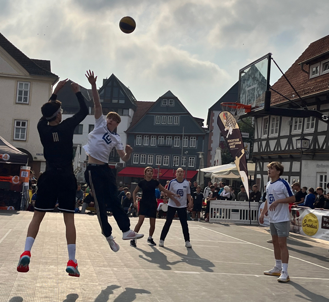 Schüler auf Basketballplatz, fliegender Ball, der nicht abgewehrt werden konnte, springende Schüler