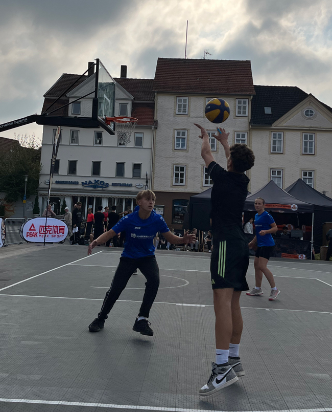 Schüler wirft Ball auf den Basketballkorb, anderer versucht ihn noch abzuwehren