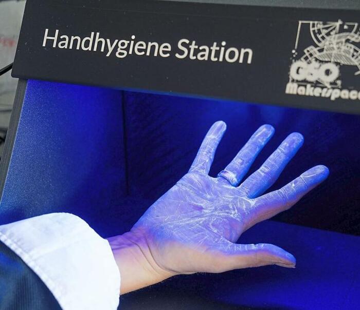 Hand unter einer Box, die lila leuchtet und auf der Hand weiße Stellen zeigt