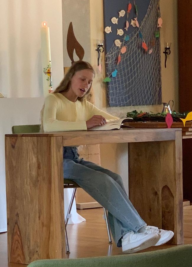 Schülerin sitzt an einem Tisch und liest aus einem Buch vor