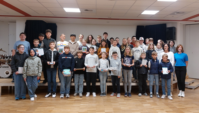 Gruppenbild mit allen Teilnehmern in der Aula, Schüler halten Urkunden und Preise in der Hand