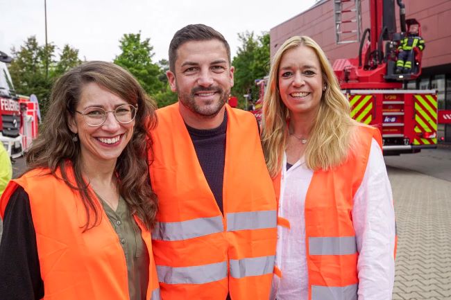 Nahaufnahme von drei Personen in orangenen Warnwesten auf dem Schulhof stehend