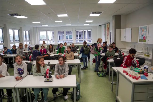 Blick in einen Klassenraum mit Schülern, die an Tischen mit Mikroskopen sitzen