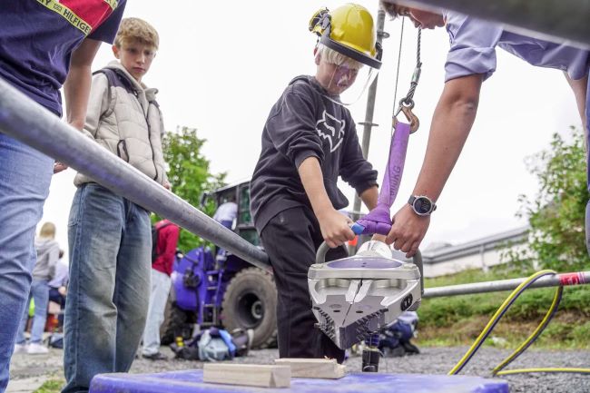 Schüler darf mit Hilfestellung eine große Schere des THW bedienen