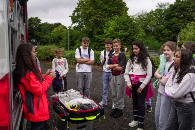 Sanitäterin erklärt Schülern etwas vor einem Rettungswagen