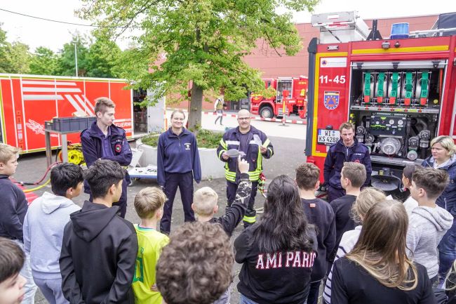 Feuerwehrleute erklären Schülern vor Fahrzeugen stehend etwas