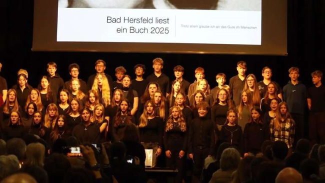 Chorschüler singend auf der Bühne vor großer Leinwand mit Bild von Anne Frank