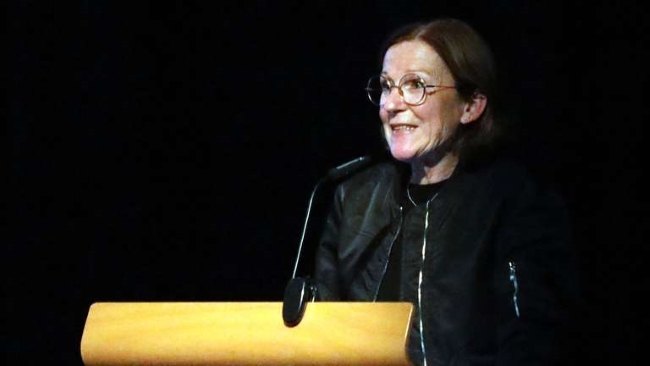 Frau hinter dem Pult zum Publikum sprechend