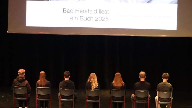 Schüler auf Stühlen auf der Bühne sitzend mit Rücken zum Publikum