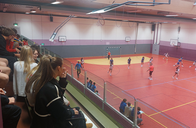 Blick von Tribüne auf Spielfeld, Schüler schauen zu wie Handballer spielen