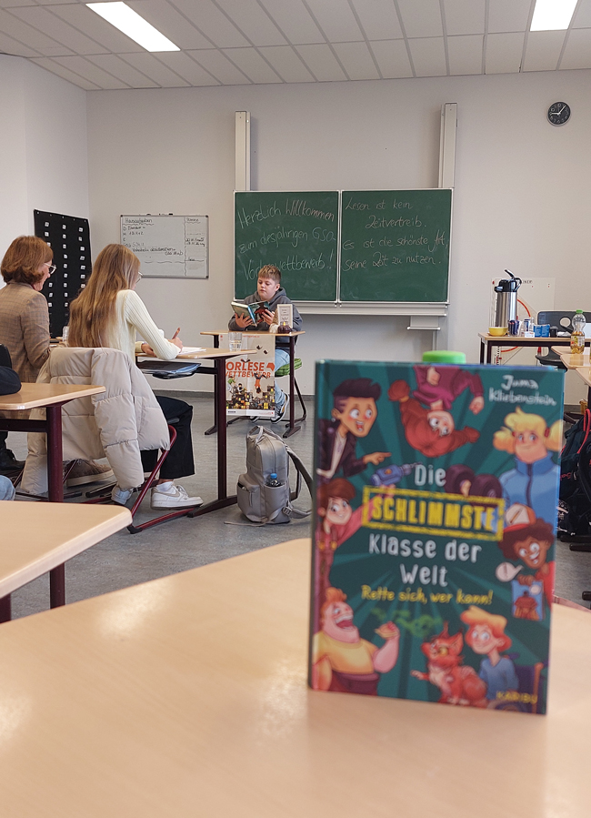 Schüler an einem Tisch in einem Klassenraum sitzend und lesend, vor ihm die Jury