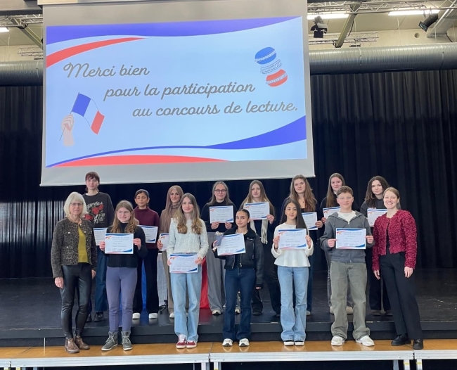 Zwei Lehrerinnen und zahlreiche Schüler auf der Bühne mit Urkunden in den Händen vor einer Leinwand