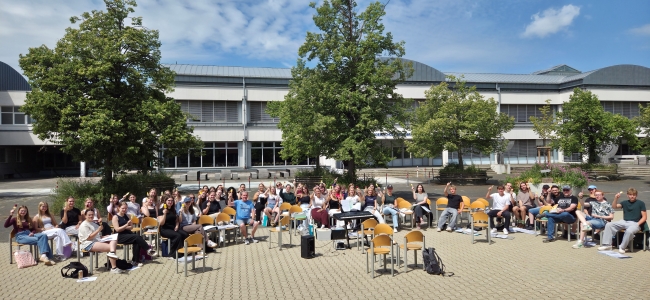 Schüler auf Stühlen auf dem Schulhof vor dem Schulgebäude mit Eis in der Hand
