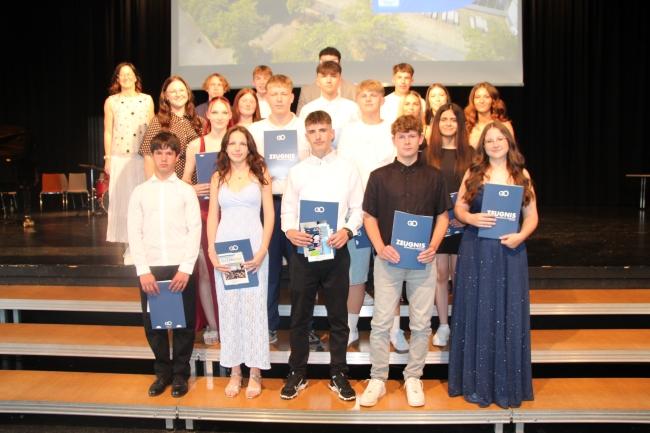 Gruppenfoto einer Schülergruppe mit Zeugnissen und Klassenlehrer