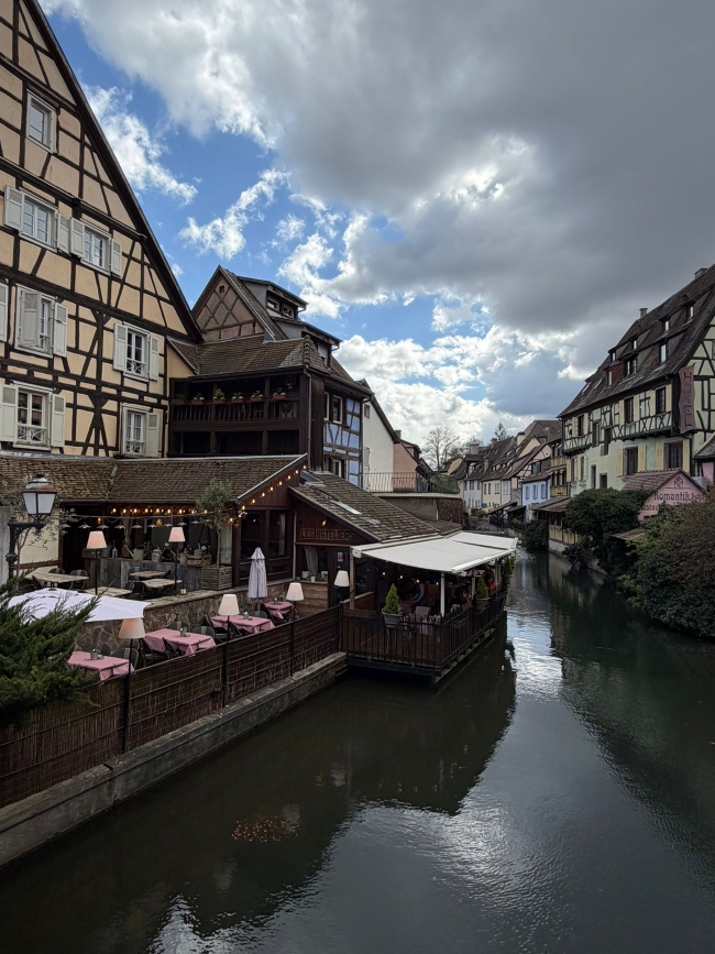 Blick auf einen Fluss, der durch eine Stadt führt und an dem dicht am Wasser Fachwerkhäuser stehen