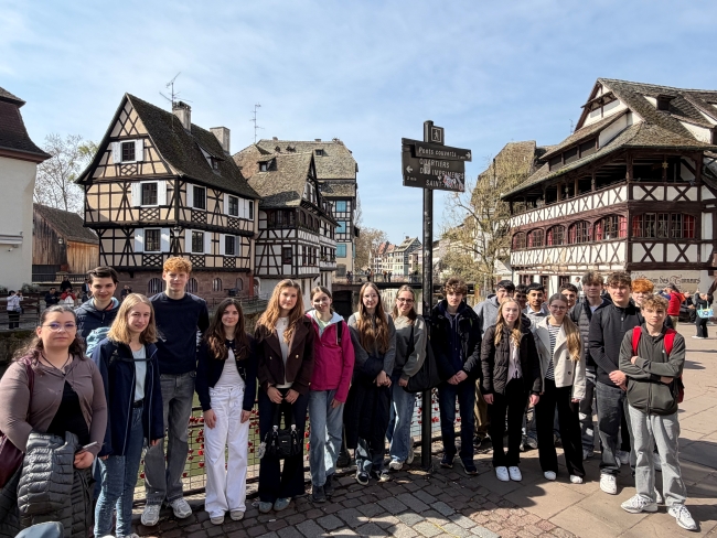 Schüler vor einem Geländer stehend, im Hintergrund wunderschöne Fachwerkhäuser und blauer Himmel