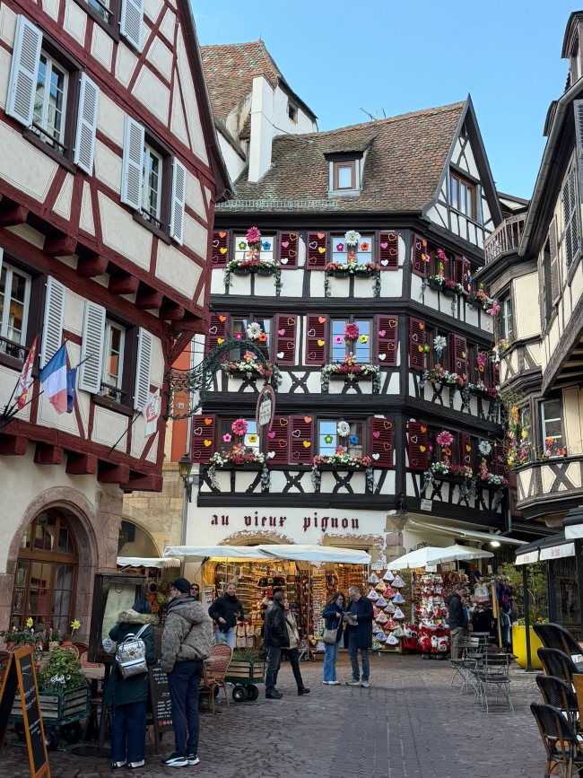 Blick auf ein großes, mit bunten Herzen geschmücktes Fachwerkhaus in einer Straße mit Läden und Menschen, die dort bummeln