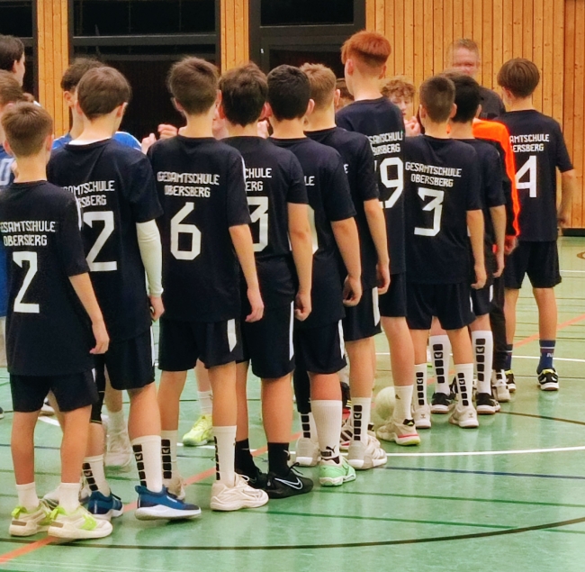 Sporthalle, Schüler mit Trikots in einer Reihe stehend von hinten zu sehen, Trikots sind dunkelblau mit weißen Nummern und der Aufschrift Gesamtschule Obersberg