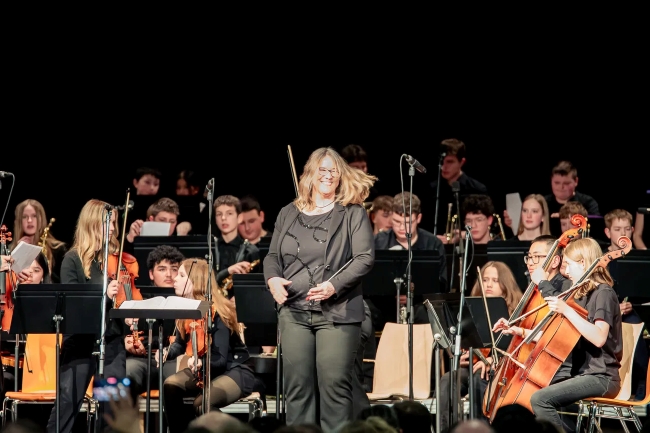 Lehrerin glücklich lachend vor ihrem Orchester auf der Bühne