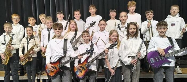 Gruppenbild Nahaufnahme von Schülern mit Blasinstrumenten und Gitarren, alle mit weißem Oberteil bekleidet, lächeln in die Kamera