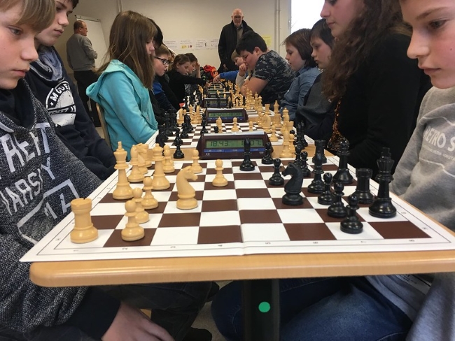 Schüler sitzen sich an Schachbrettern an mehreren Tischen hintereinander gegenüber und schauen konzentriert auf das Spiel