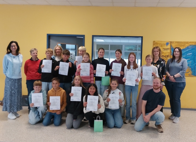 Gruppenbild mit Schülern und Lehrern vor einem Klassenzimmereingang, Schüler halten Urkunden vor sich